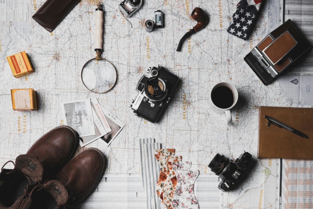 Assorted travel items, including cameras, map, boots, pipe, magnifying glass, coffee cup, notebook, film, and vintage photos arranged on a surface—perfect essentials for international visitors seeking practical travel information about Boljoon Cebu.
